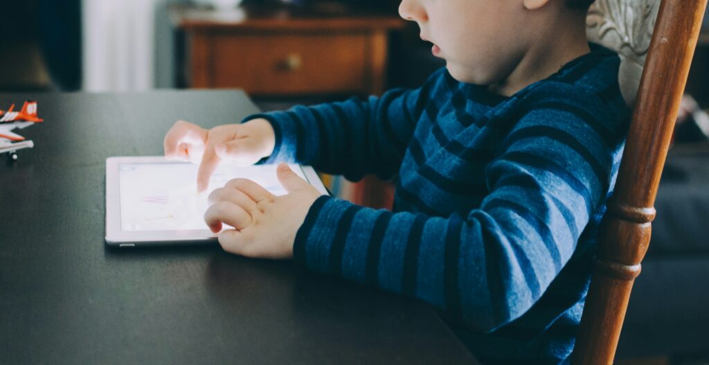 little boy sitting at a table playing on a tablet